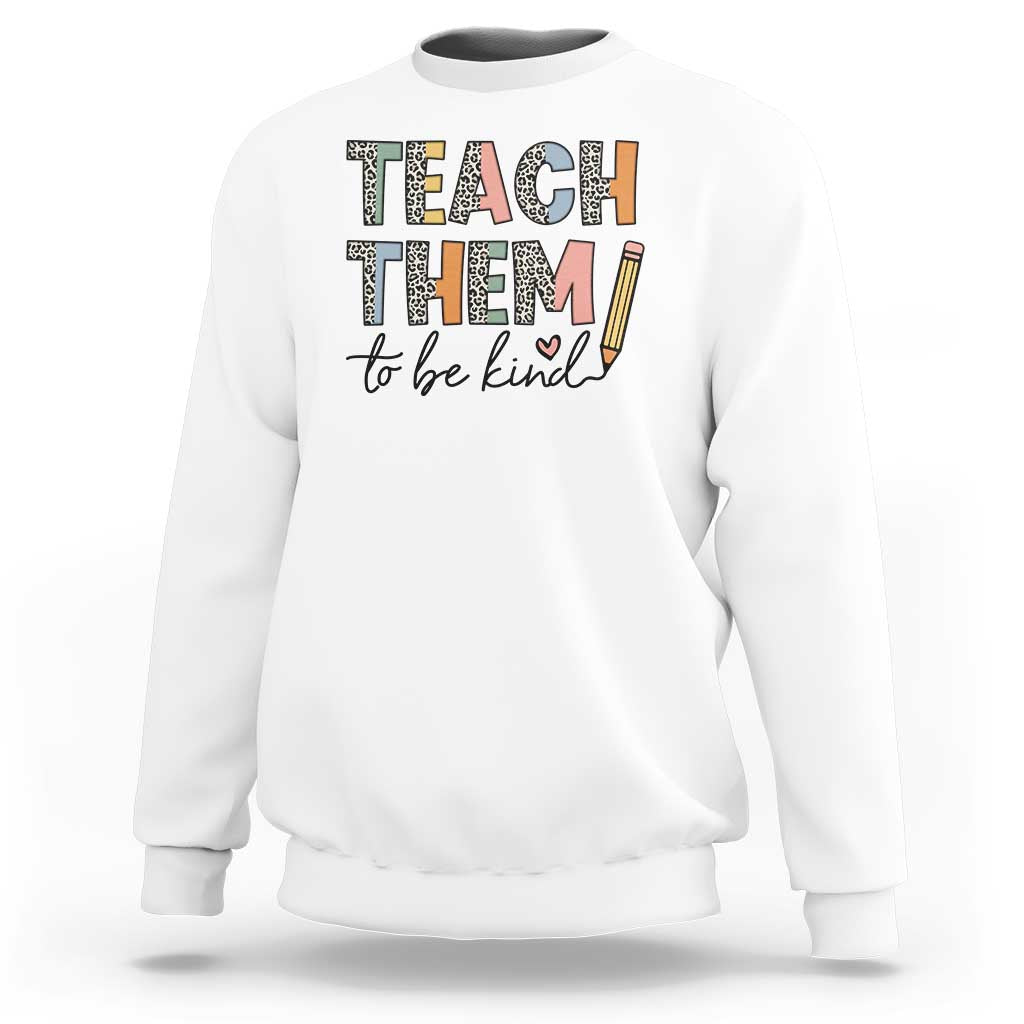 White teacher sweatshirt with “Teach Them” and “to be kind” pencil-style graphic.