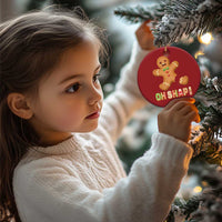 Child beside a round red gingerbread Christmas ornament with gold string and "OH SHAPI!"