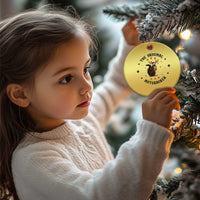 Gold round Christmas ornament with nutcracker squirrel graphic hanging on a small child.