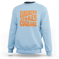 Light blue sweatshirt with orange 'Kindness Takes Courage' graphic on front.