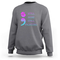Dark heather crewneck sweatshirt with “STILL HERE STILL FIGHTING” graphic and semicolon symbol