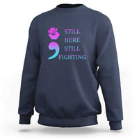 Navy crewneck sweatshirt with “STILL HERE STILL FIGHTING” graphic and semicolon symbol