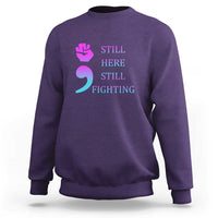 Purple crewneck sweatshirt with “STILL HERE STILL FIGHTING” graphic and semicolon symbol
