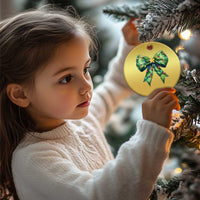 Round gold Christmas ornament with green bow and gold star, held by a child near the tree.