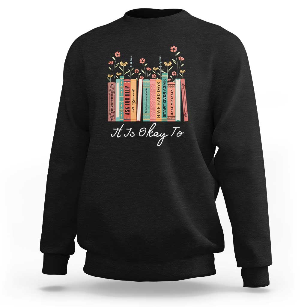 Dark gray crewneck sweatshirt with colorful floral book graphic and “It is okay to” text