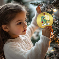 Gold round hanging ornament with Tree Rex dinosaur graphic, held near a Christmas tree