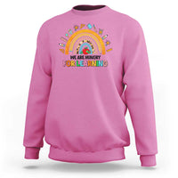Magenta crewneck sweatshirt with rainbow and “We are hungry for learning” graphic