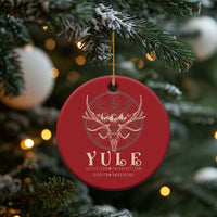 Red round Christmas ornament with gold hanging string and antlered skull emblem on tree.
