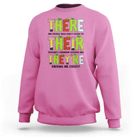 Pink sweatshirt with colorful “THERE/THEY’ grammar text graphic on the front, crew neck