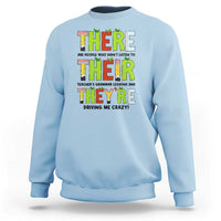 Light blue sweatshirt with colorful “THERE/THEY’ grammar text graphic on the front, crew neck
