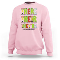 Pink sweatshirt with colorful “THERE/THEY’ grammar text graphic on the front