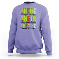 Purple sweatshirt with colorful “THERE/THEY’ grammar text graphic on the front, crew neck