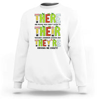 White sweatshirt with colorful “THERE/THEY’ grammar text graphic on the front, crew neck