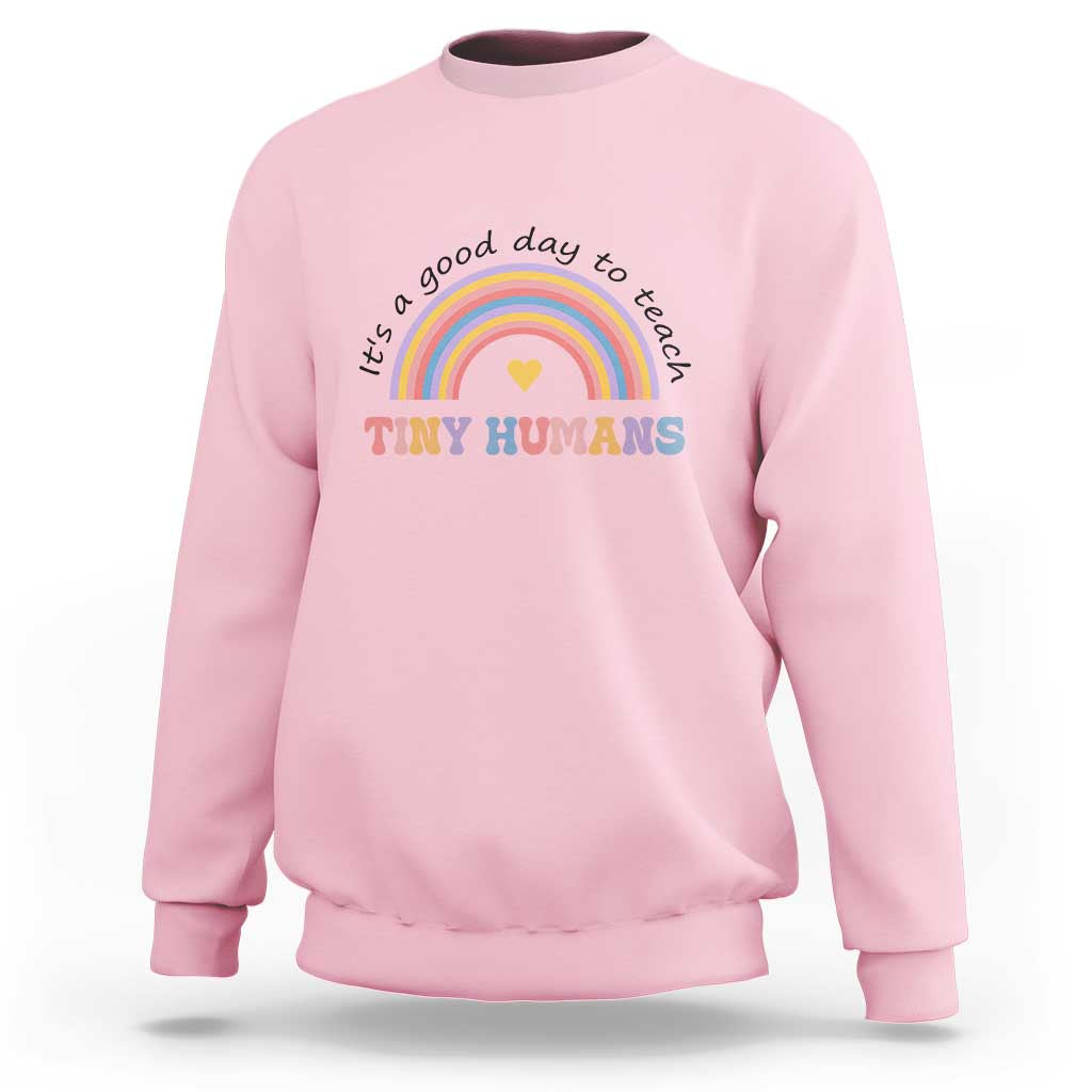 Pink sweatshirt with rainbow arc and heart graphic reading "Tiny Humans"