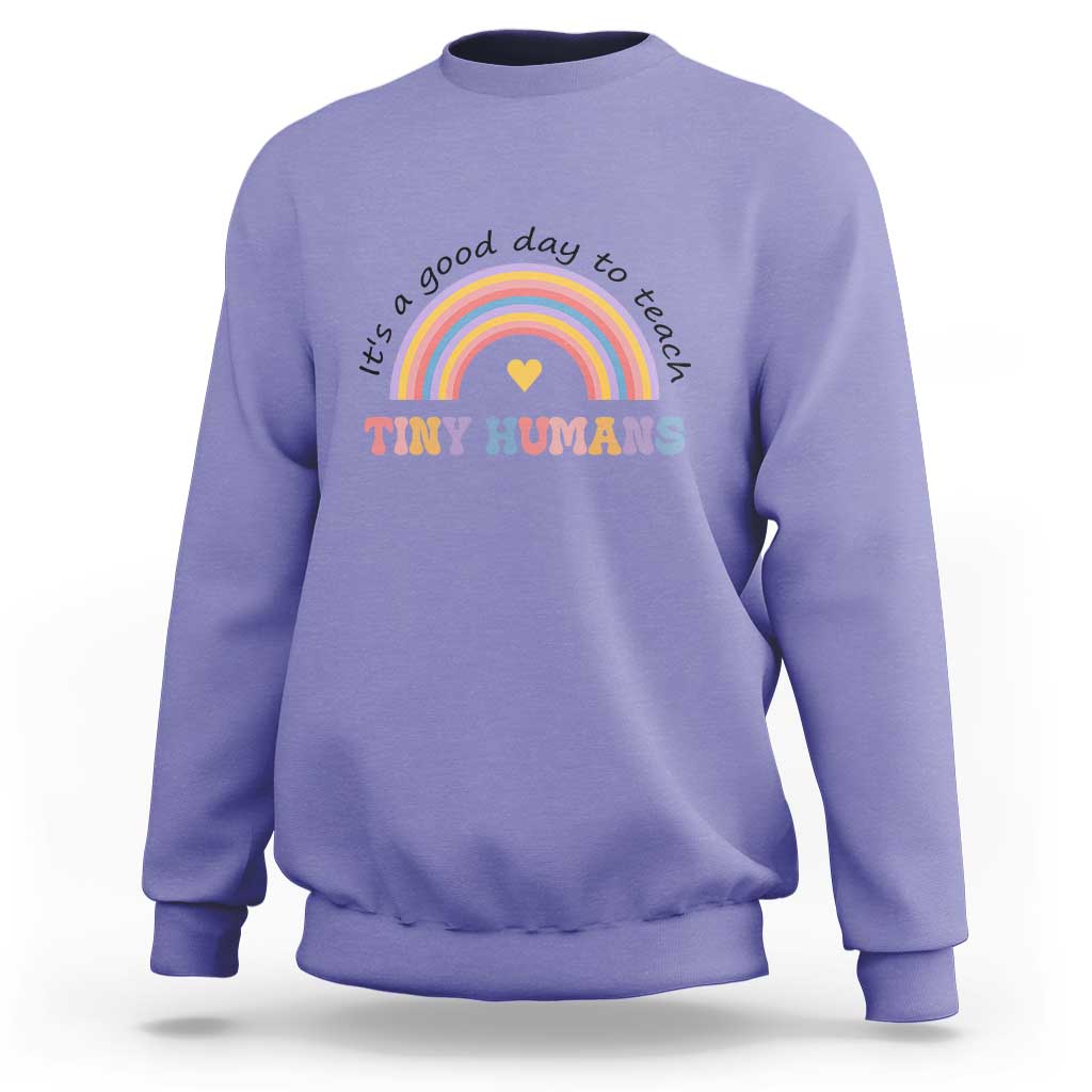 Purple sweatshirt with rainbow arc and heart graphic reading "Tiny Humans"