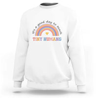White sweatshirt with rainbow arc and heart graphic reading "Tiny Humans"