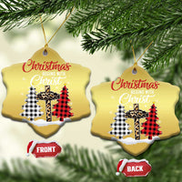 Two gold heart-shaped Christmas ornaments hanging from evergreen branches with plaid cross design