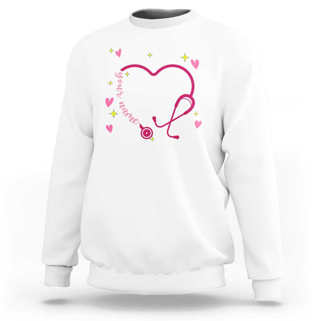 White crewneck sweatshirt with pink heart stethoscope graphic and multicolor heart details