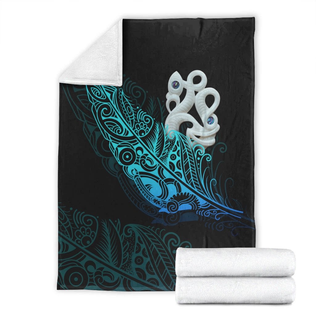 Folded black blanket with teal fern pattern and white manaia emblem