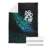 Folded black blanket with teal fern pattern and white manaia emblem