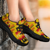 Yellow sneakers on feet with red, black, and yellow geometric tribal pattern