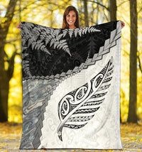 White blanket held outdoors: black fern texture, gray blocks, and feather emblem on right side