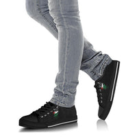 Black low-top sneakers on feet with jeans, black laces, green/red graphic