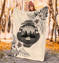 Beige Costa Rica blanket held outdoors, featuring central emblem and palm hibiscus print