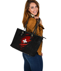 Black grunge-style leather tote with red Swiss cross center design, zip-top and wide profile