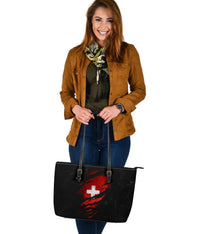 Black leather tote with red Swiss cross emblem, zip-top edge and adjustable shoulder straps