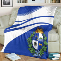 Blue and white Uruguay-style blanket with diagonal stripes and central crest emblem.