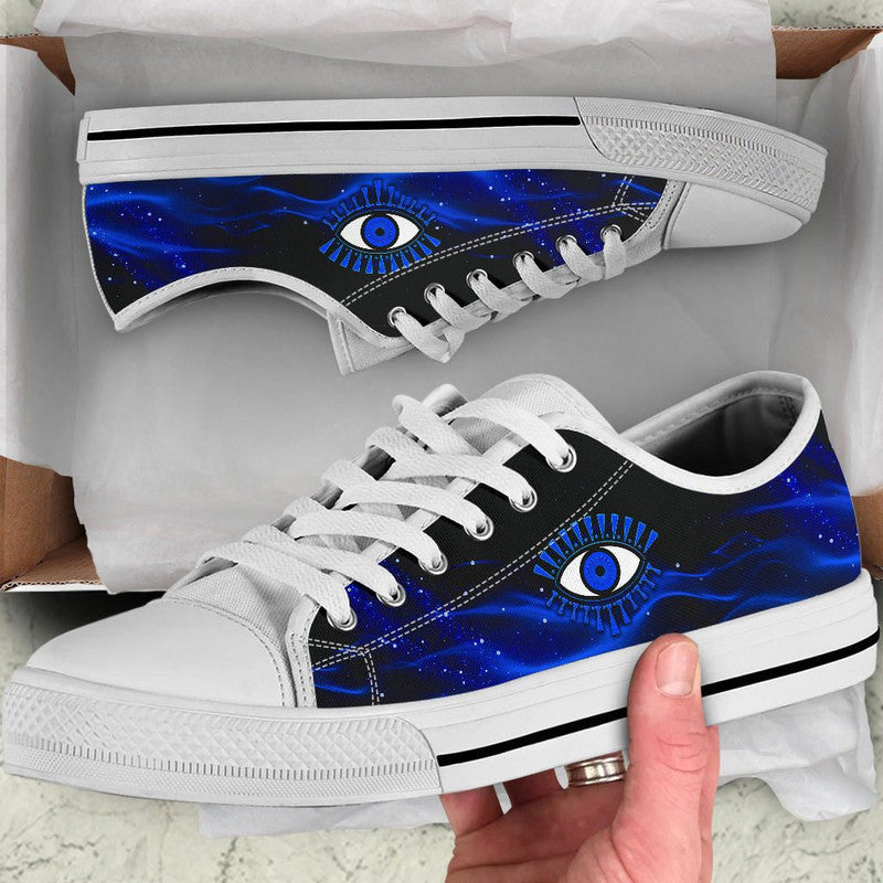 White and black low top sneakers with blue evil eye graphic and white laces.