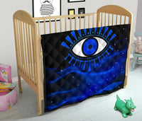 Blue evil eye quilt draped on a light wood baby bed, black top panel with stitching