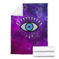 Purple evil eye blanket folded over white towels, featuring blue eye design.