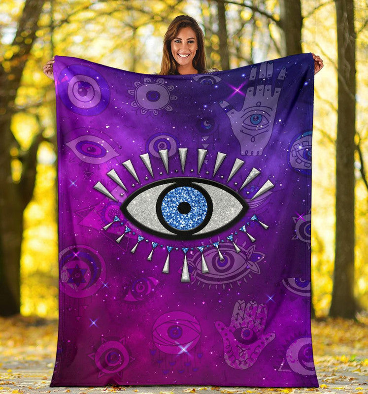 Purple throw blanket with blue evil eye motif held by smiling person outdoors.
