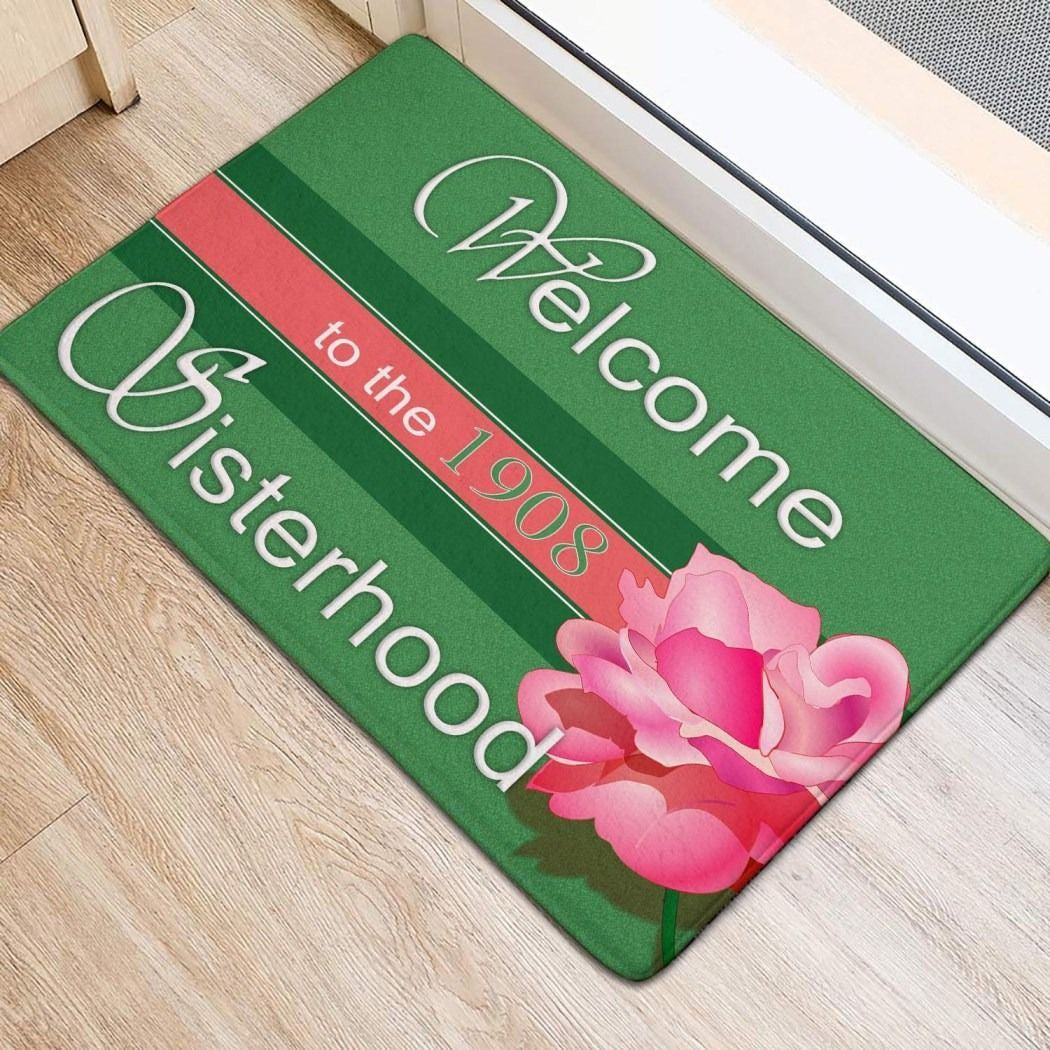 Green door mat: 'Welcome', 'to the 1908', 'Sisterhood' with pink flowers