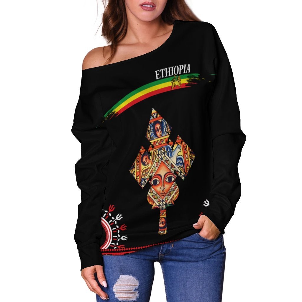 Black off-shoulder sweater with central Ethiopian cross portrait graphic and rainbow stripe
