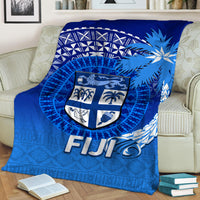 Folded blue Fiji tapa blanket with shield crest and coconut-tree icons, “FIJI” text