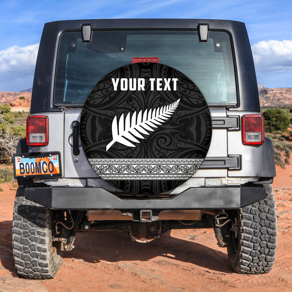 Black circular spare tire cover with white fern and swirl pattern, 'YOUR TEXT' center