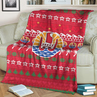 Red Christmas blanket draped on couch featuring Tahiti drum emblem, palm trees, stars, and green trim