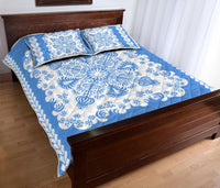 Folded corner view of blue quilt bed set with white swirls, flowers, and diagonal border