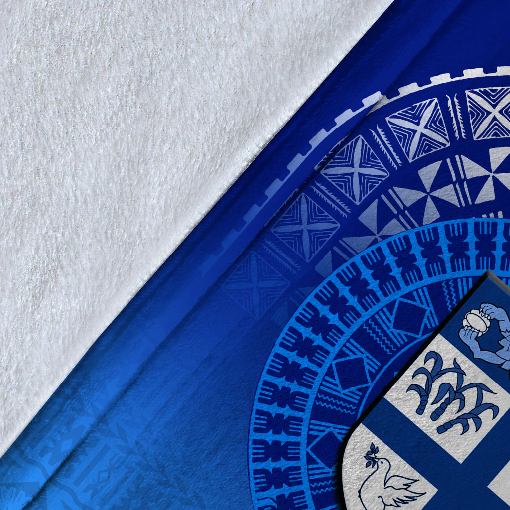 Close-up of blue blanket edge with white border, tapa pattern, and shield emblem detail