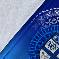 Close-up of blue blanket edge with white border, tapa pattern, and shield emblem detail