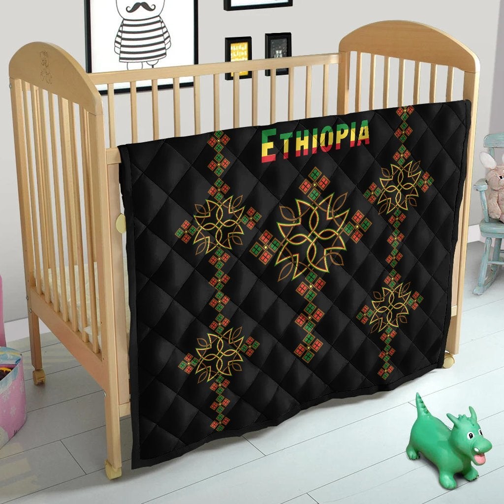 Black quilt on wooden crib, diamond quilted squares with colorful geometric cross motifs