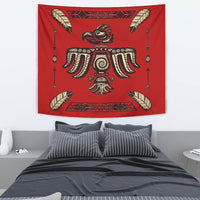Red tapestry showing native bird with feather wings, central tribal figure and arrows