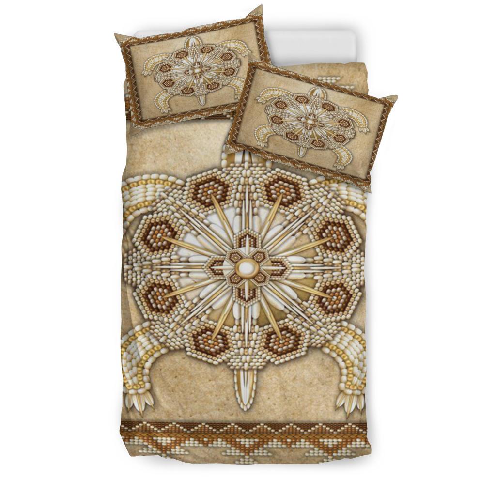 Studio view of tan bedding set with beaded turtle symbol panel and two pillows