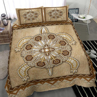 Close view of tan bedspread with large beaded turtle symbol and two patterned pillows