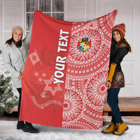 Red Tongan crest blanket with white geometric ngatu pattern, held by two people