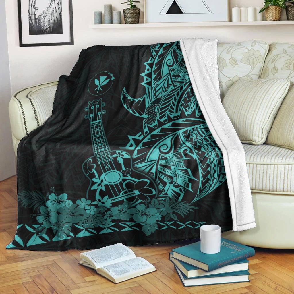 Black and turquoise Hawaiian blanket with ukulele and floral tiki motifs, draped on sofa
