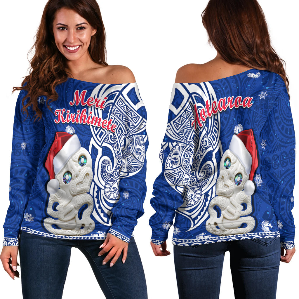 Blue off-shoulder sweater with white tiki graphic, holiday lettering, and snowflake motifs